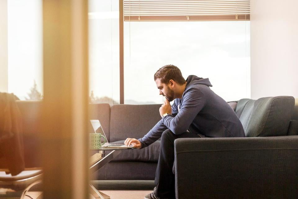 Mann der von zu Hause aus auf dem Sofa arbeitet